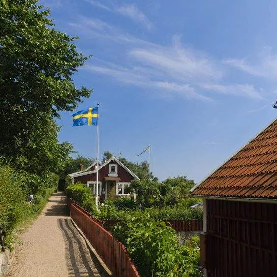 Grusväg med svensk flagga och röd stuga en sommardag